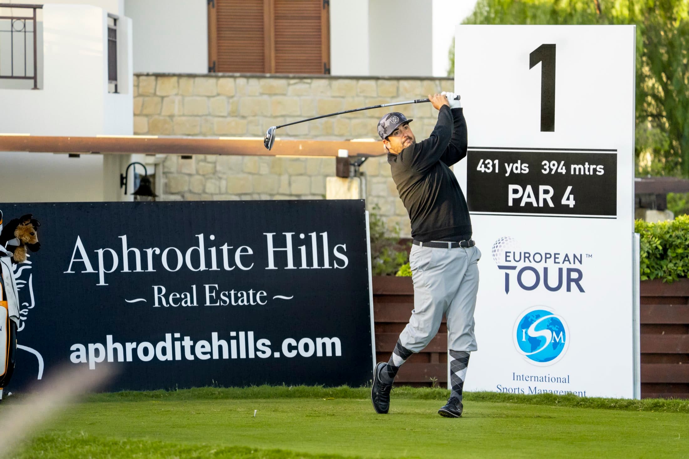 A player tees off at Aphrodite Hills during the 2020 European Tour, framed by the European Tour and Aphrodite Hills signage, captured by Backlight Media