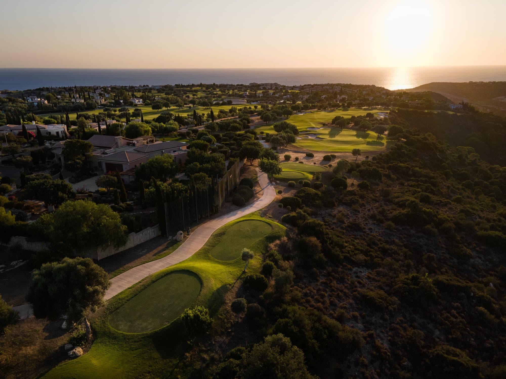 Golden-hour aerial of the renovated Aphrodite Hills golf course running to the sea, documented by Backlight Media