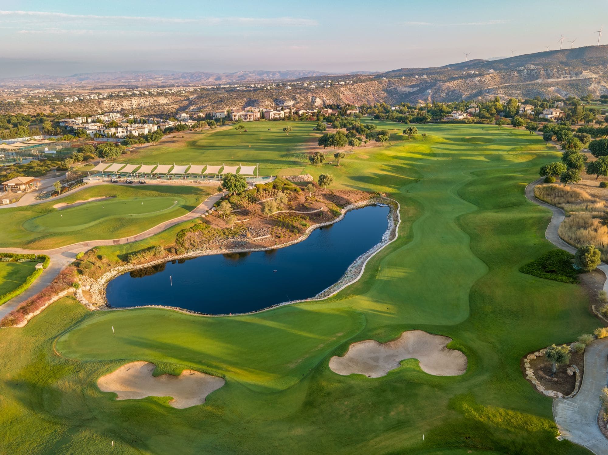 Aerial vista of the renovated Aphrodite Hills course with lake and bunkers, documented by Backlight Media