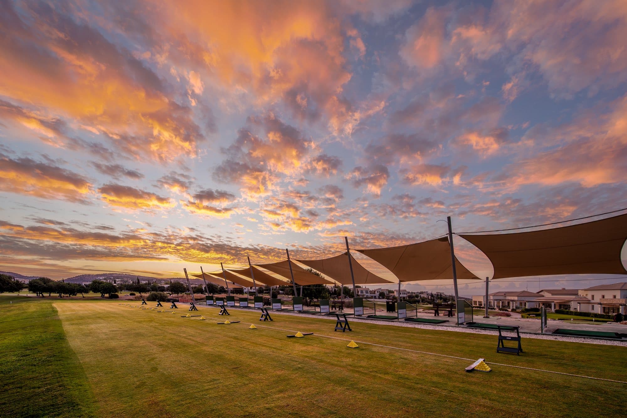 The driving range at Aphrodite Hills under a vivid sunset sky, captured by Backlight Media