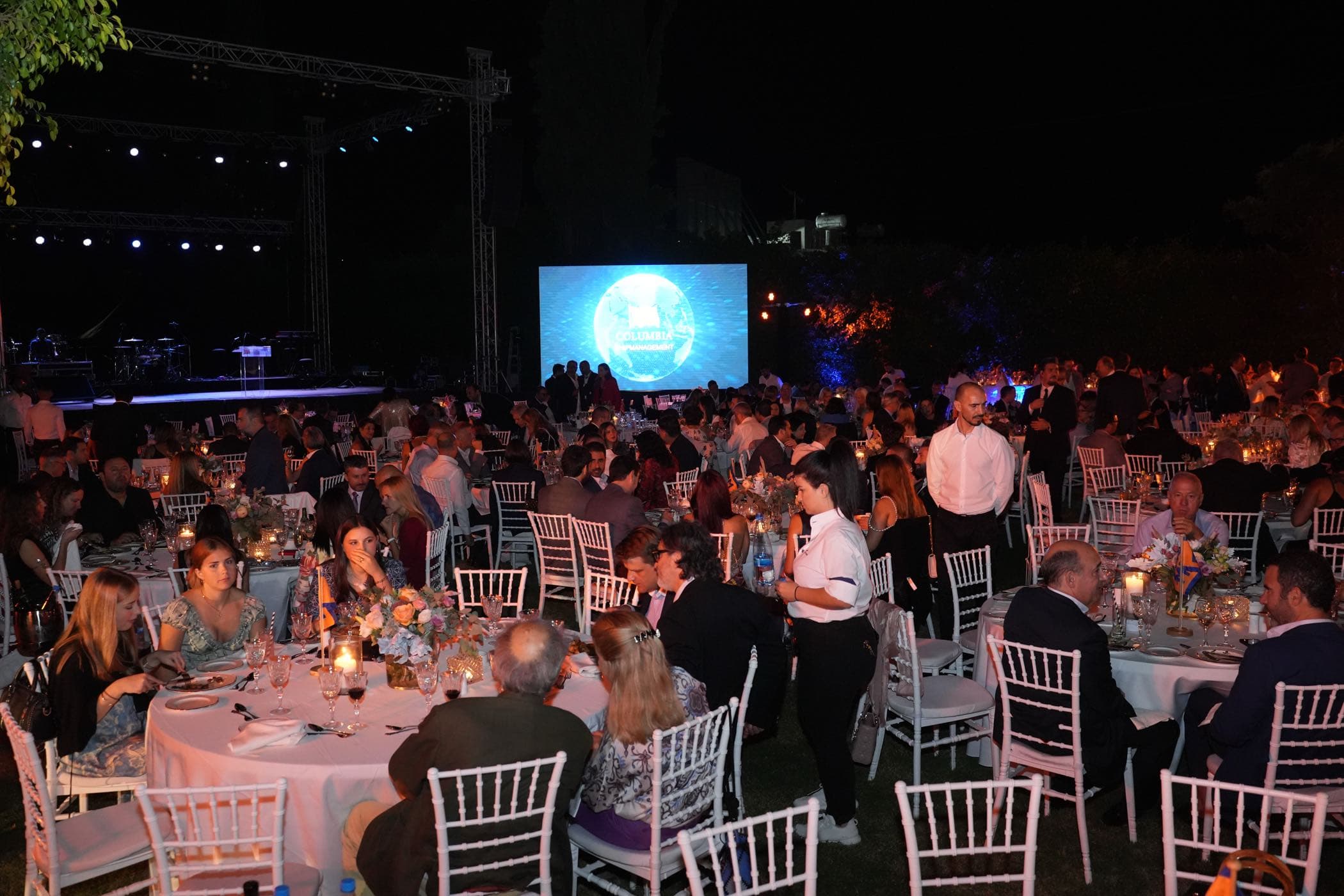 Wide view of the Columbia Group gala dinner with stage and branded screen, produced and captured by Backlight Media