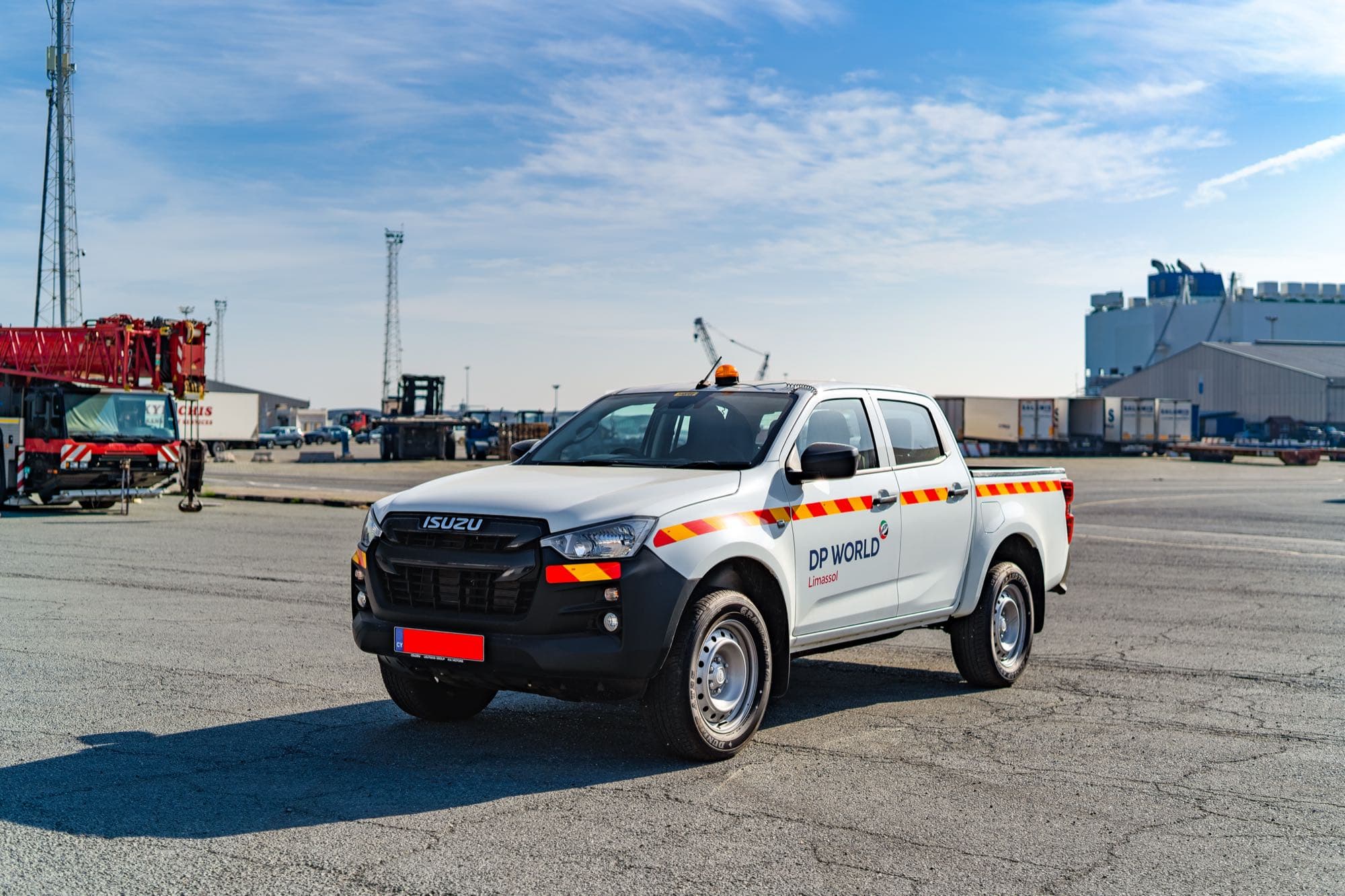 A white DP World Limassol Isuzu D-Max fleet pickup on the port apron with a RoRo car-carrier ship and a red mobile crane behind, by Backlight Media
