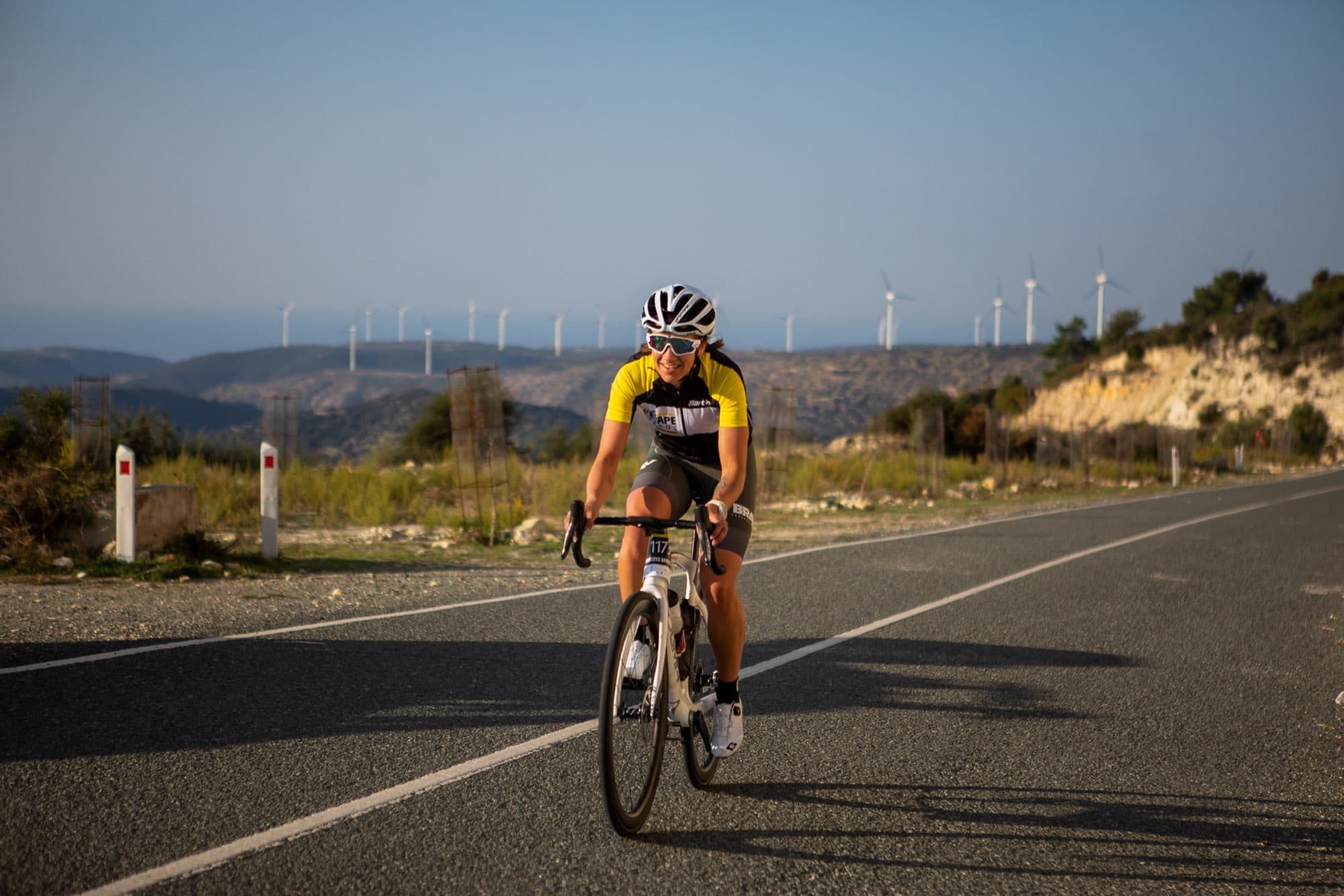 A cyclist rides the coast road past wind turbines and the sea at L'Étape Cyprus, the Tour de France race, captured on the day by Backlight Media in Cyprus