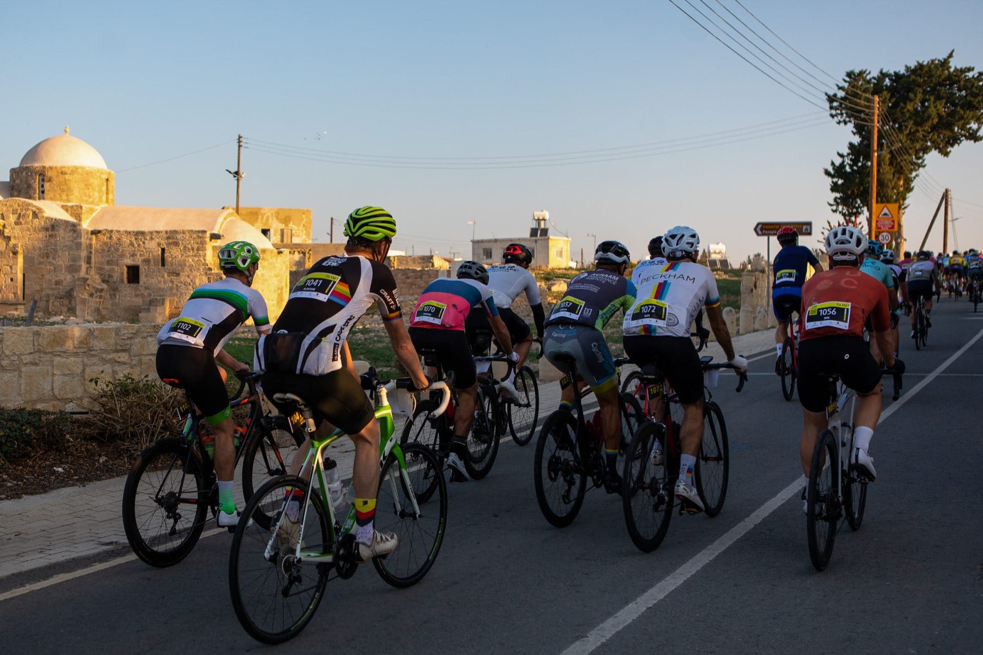 The peloton rides past a domed Cypriot church at golden hour during L'Étape Cyprus, the Tour de France race, filmed by Backlight Media in Cyprus