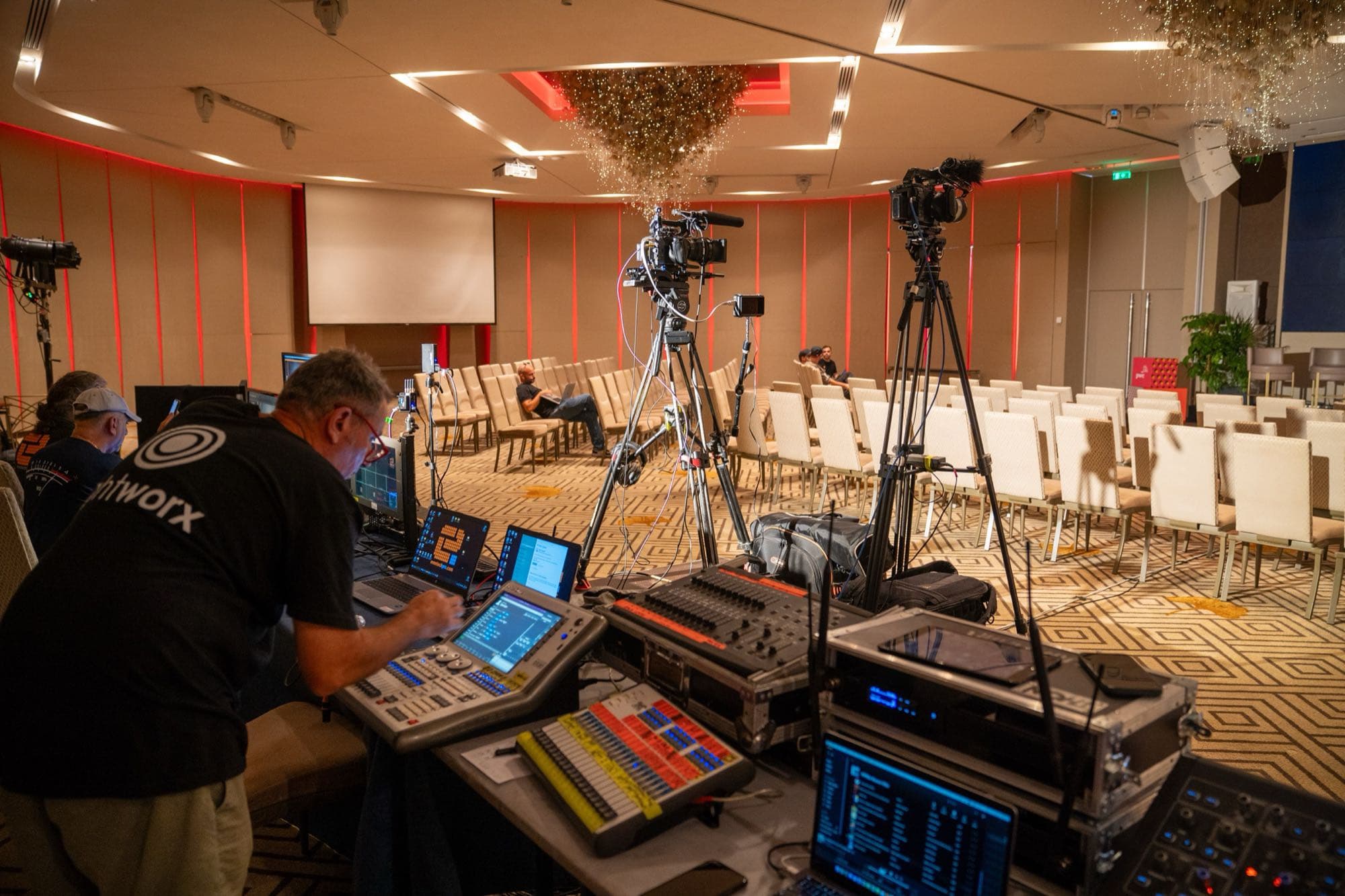 The vision-mixing control position at the PwC Annual Conference in Cyprus, mixing desk and monitors with two tripod broadcast cameras on the seating, run by the joint Backlight Media and Eventechpro team